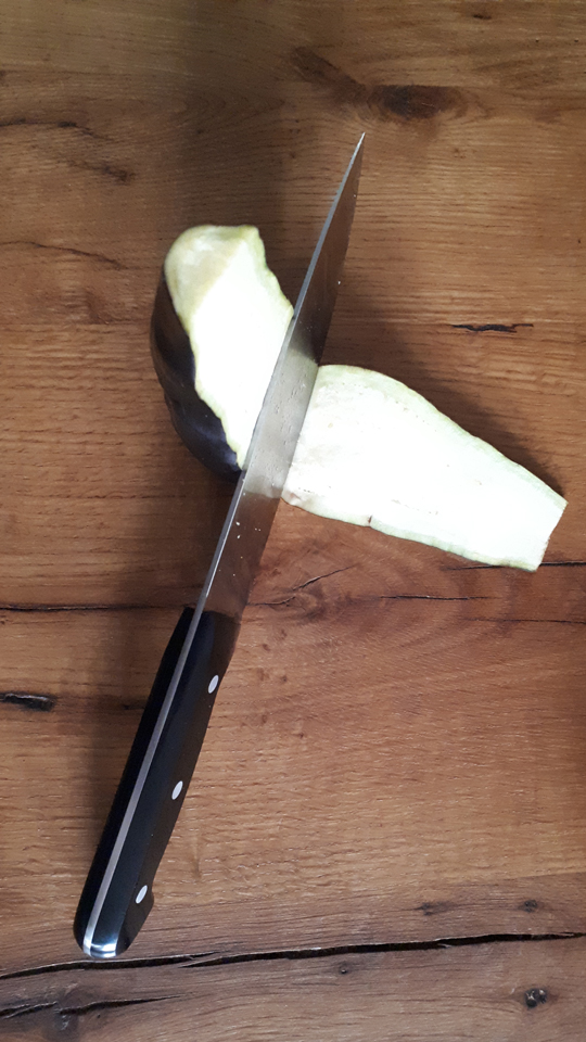 Lieblingsrezept. Aubergine, die von einem Messer in Scheiben geschnitten wird