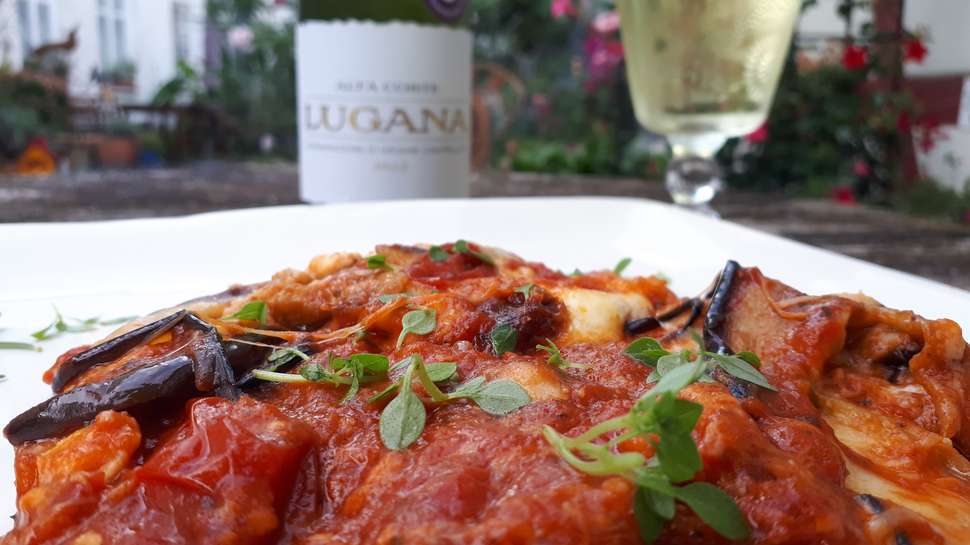 Lieblingsrezept. Die fertige Parmigiana di Melanzane. Draußen im Garten mit einem Glas Lugana