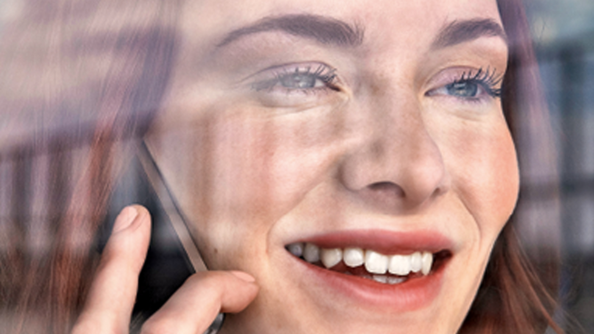 Nahaufnahme einer telefonierenden, lachenden Frau mit rotbraunen Haaren